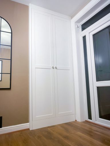 Tall white cabinet in a corner, with a mirror on the wall nearby and a window.