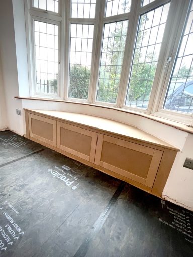 Curved wooden bench against curved window, with flooring details visible below.