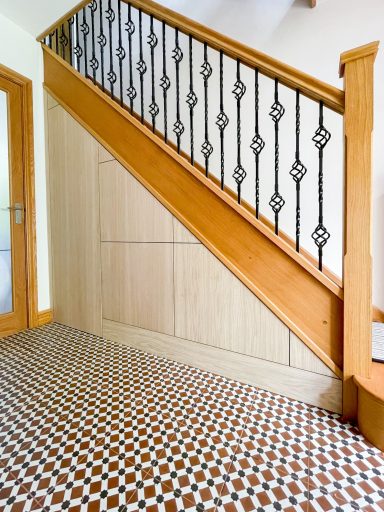 Wooden staircase with ornate black metal railing and patterned tiled floor.